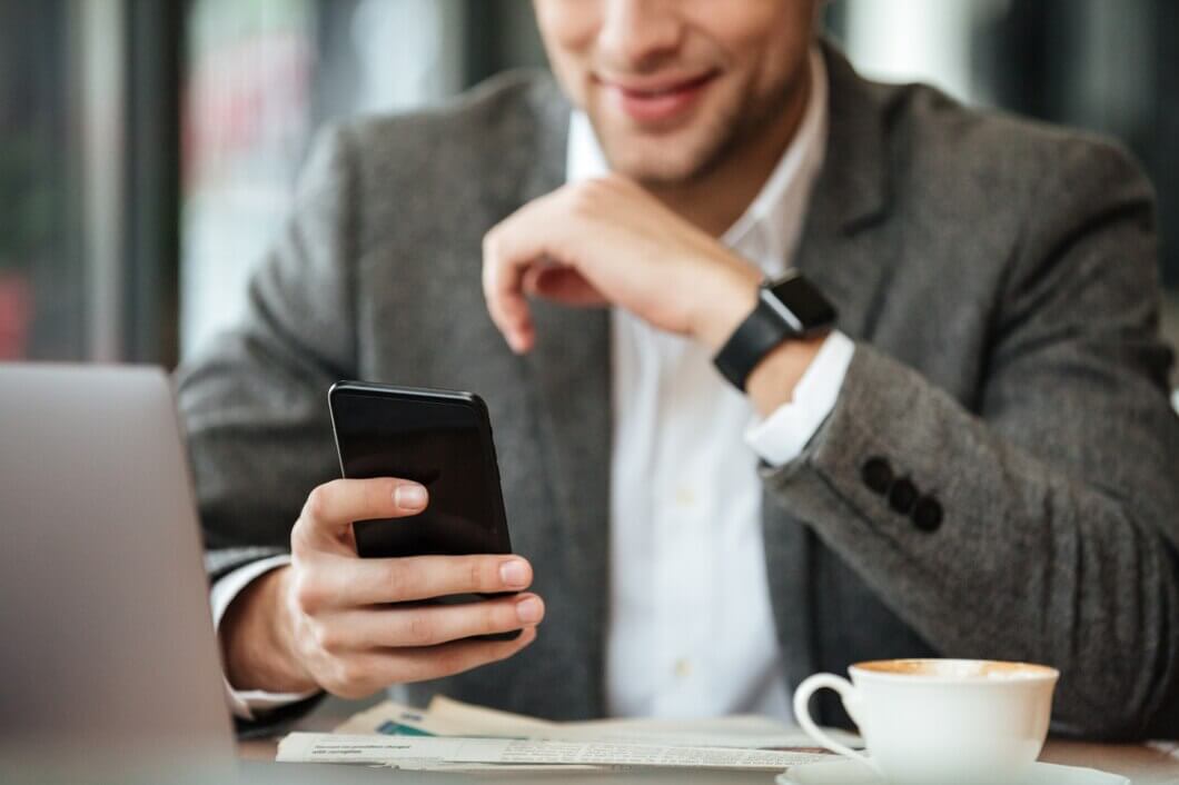 A businessman checking his phone while working on a laptop in a café