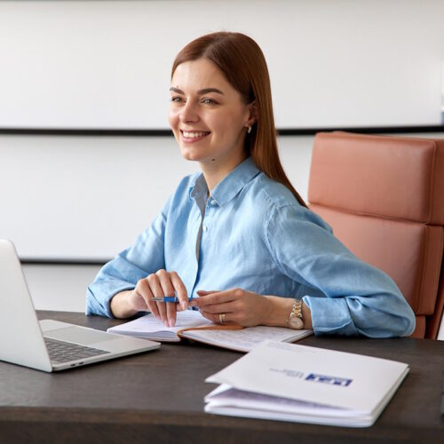 Smiling person working at a desk with a laptop and papers