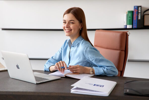Smiling person working at a desk with a laptop and papers